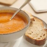 Bowl of carrot soup with slice of bread.