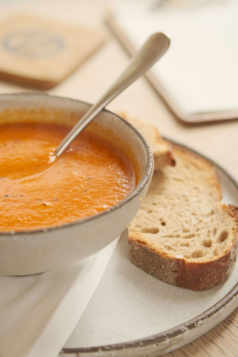 Bowl of carrot soup with slice of bread.